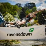A teen shemozzle competitor in an orange vest dives through the air over a 